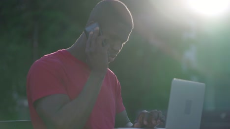 Junger-Afroamerikanischer-Mann,-Der-Auf-Dem-Laptop-Tippt-Und-Telefoniert